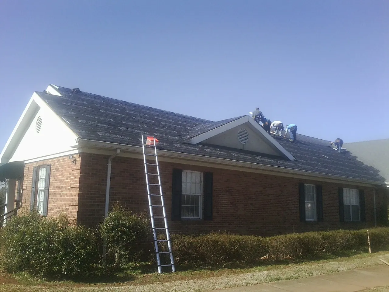 Crew tearing shingles off a brick ranch roof with a ladder set — Emergency Roof Repair work by our crew in Lupton City