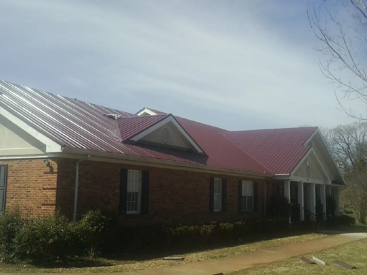 Red metal roof with gabled entries on a long brick building, from a Hail Damage Roof Repair job in Lupton City
