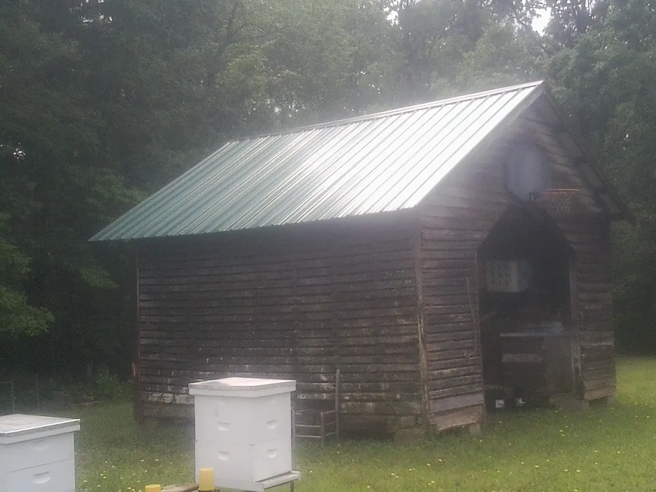 Green metal roof on a weathered barn beside stacked beehives in Lupton City