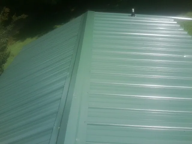 New green metal panels meeting at the ridge of a roof — Flat Roof Repair work by our crew in Lupton City