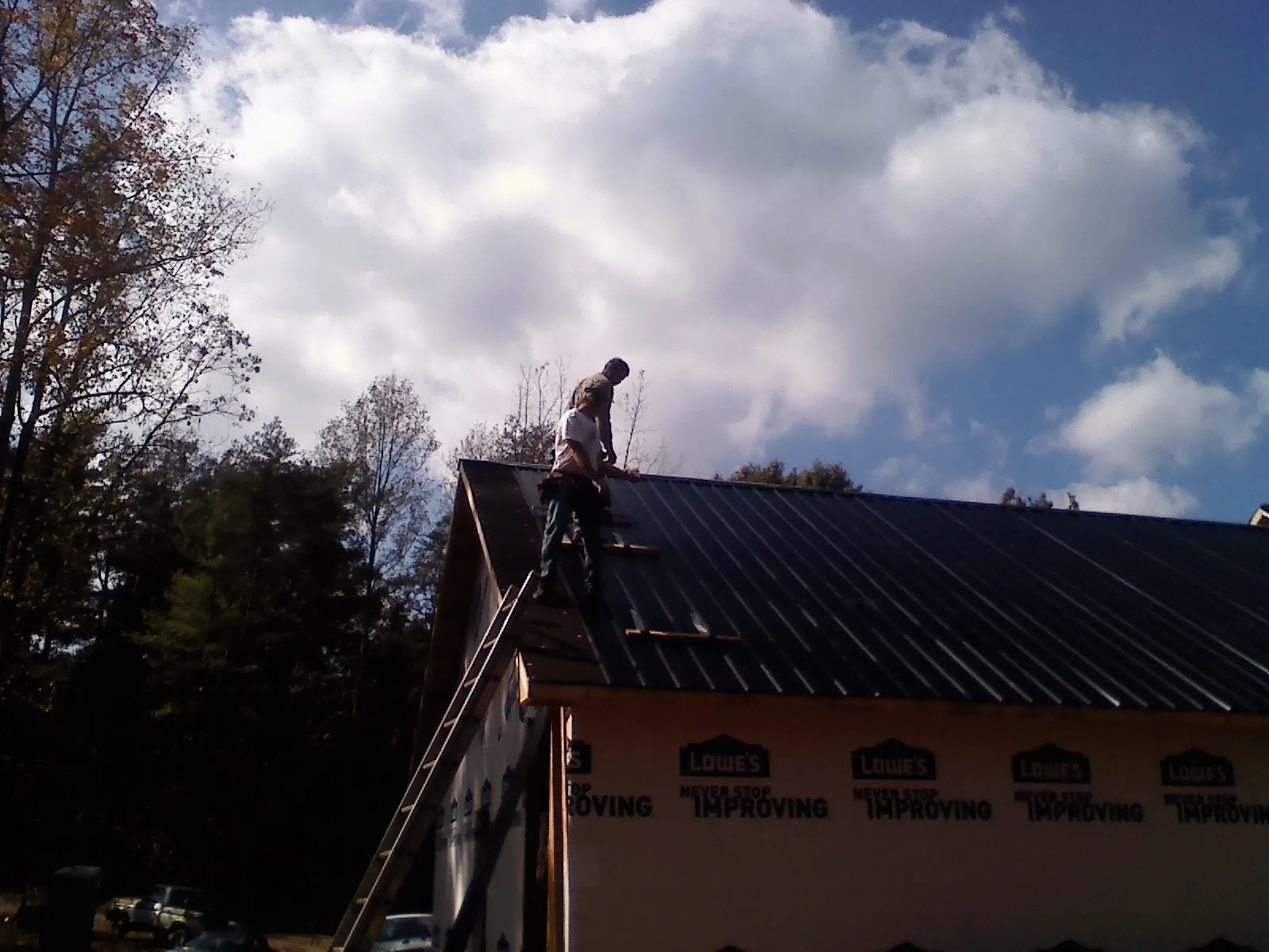 Roofer fastening dark metal panels high against a cloudy sky, from a Roof Inspection job in Lupton City