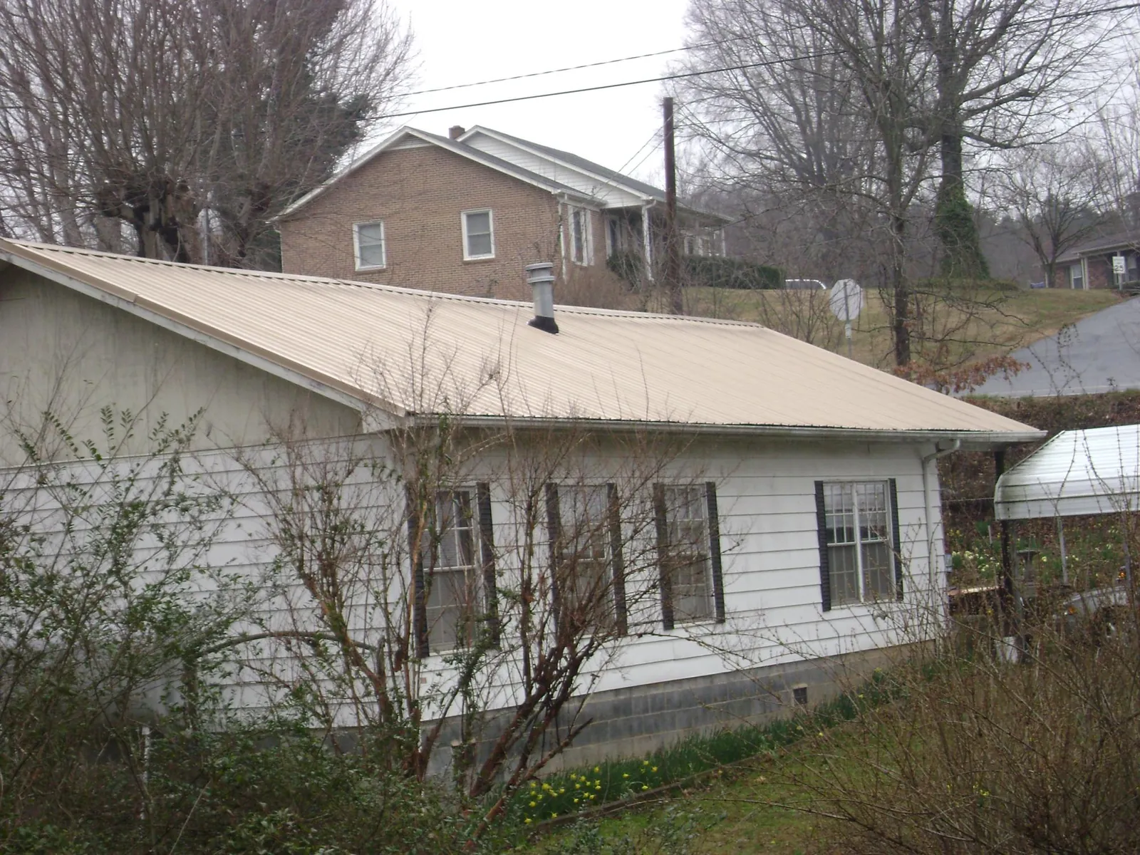 Tan metal roof on a white sided house set into a hillside — Commercial Roofing by Roofing Brothers in Lupton City